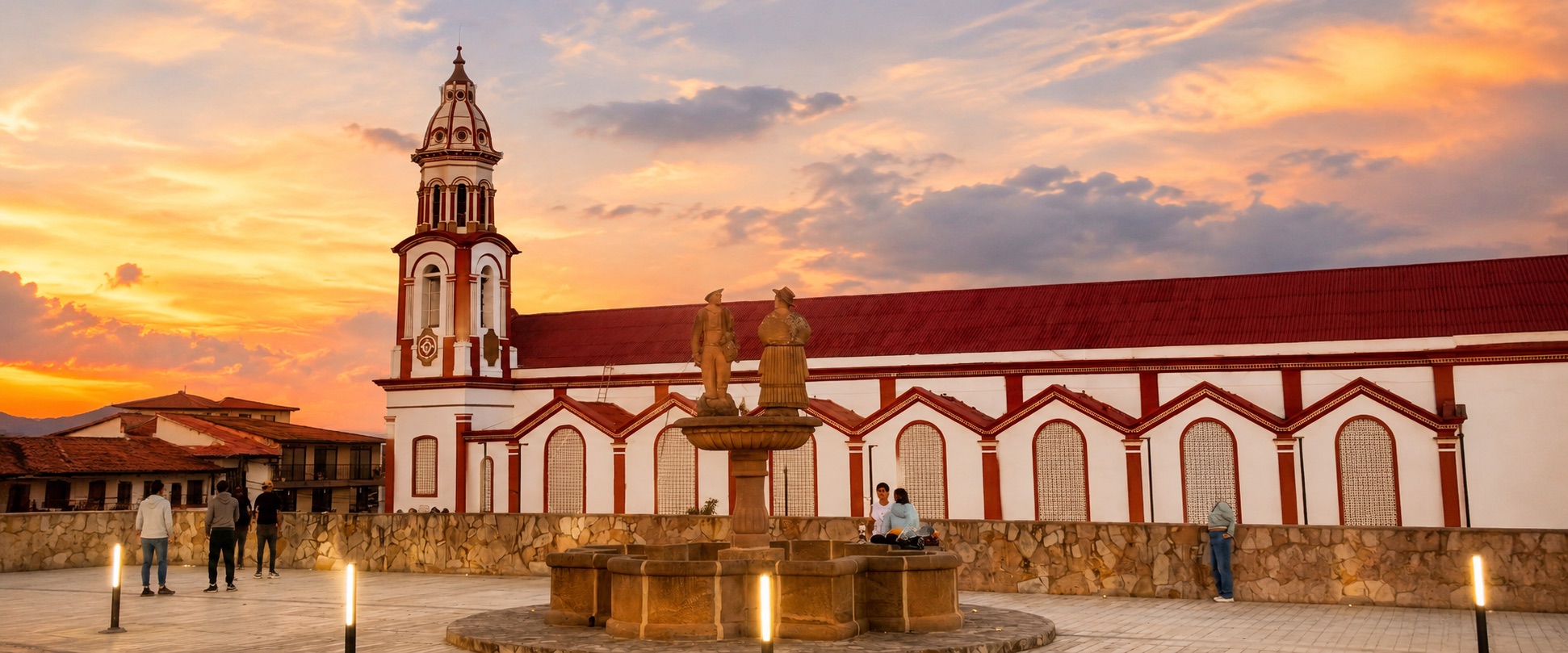 Plaza principal de Vélez, Santander, con su iglesia de fachada blanca y roja y la fuente de los danzantes al atardecer