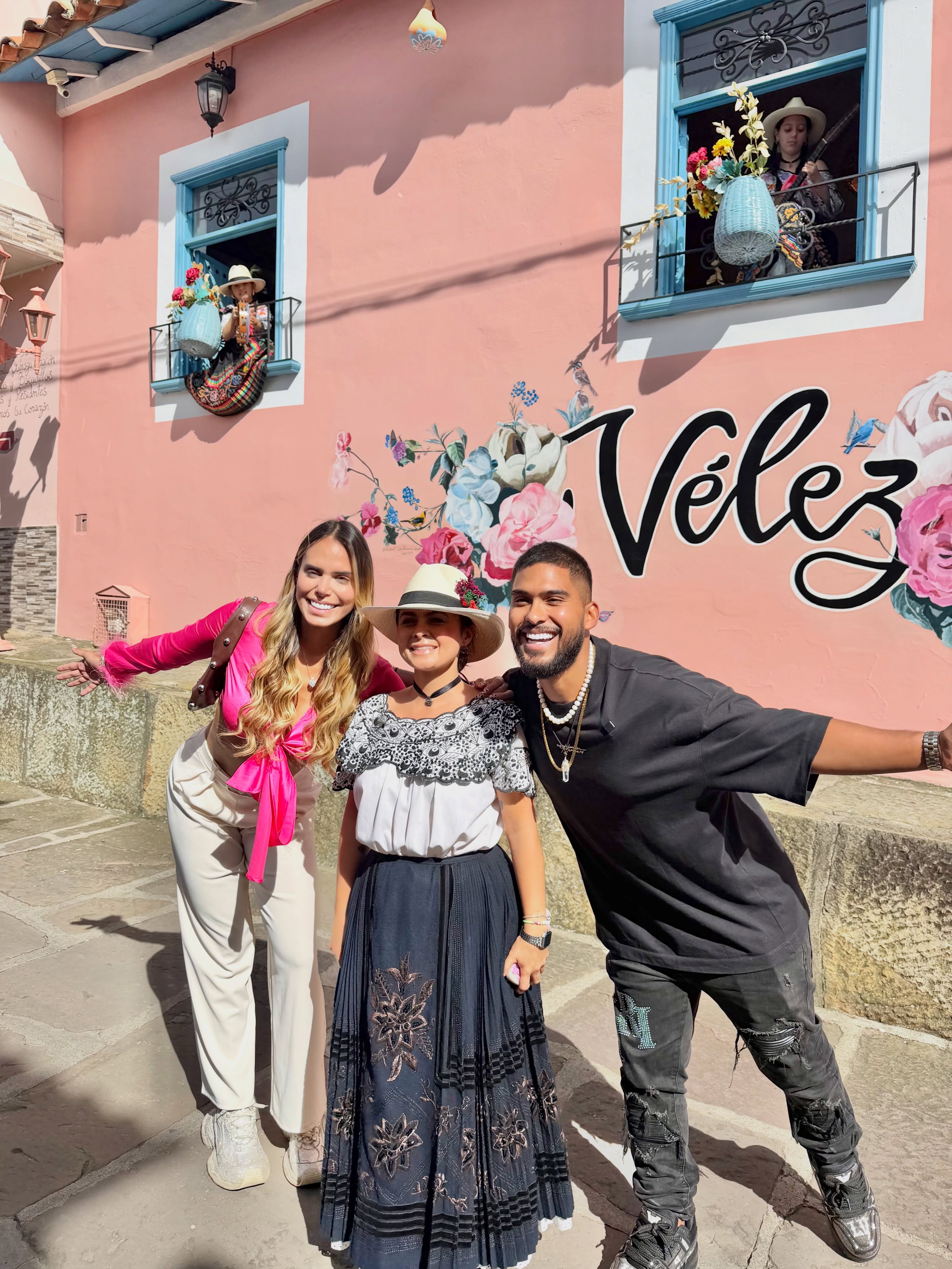 Visitantes posando frente al mural floral de Vélez en una pared color rosa